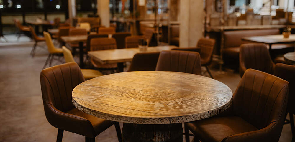 Innenraum des Hopfenfänger Restaurants mit runden Holztischen, braunen Lederstühlen und gemütlicher Bistro-Atmosphäre