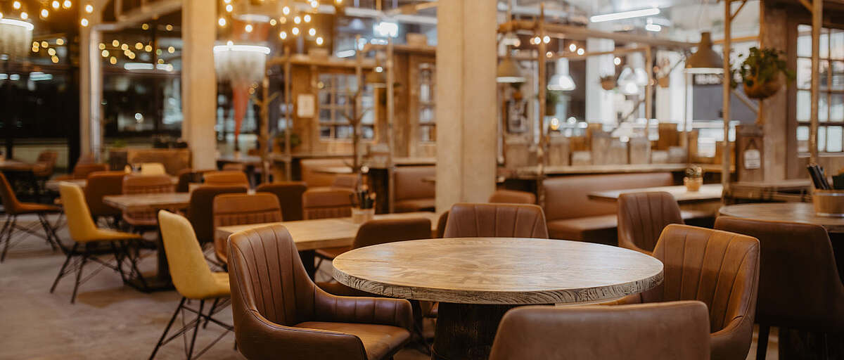 Innenraum des Hopfenfänger Restaurants in Bremen mit runden Holztischen, braunen Lederstühlen und stimmungsvoller Beleuchtung