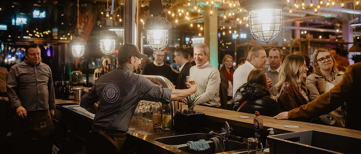 Hopfenfänger Barkeeper schenkt Bier für Gäste bei einer Feier ein – gesellige Stimmung an der Theke mit vielen Besuchern