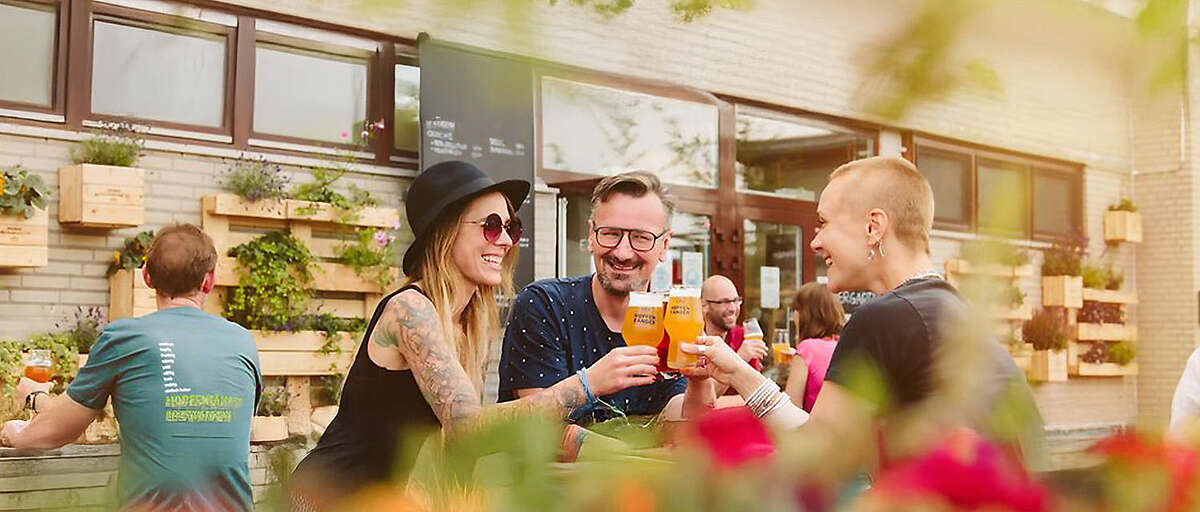 Gäste stoßen im Hopfenfänger Biergarten in Bremen mit frisch gezapftem Bier an, fröhliche Stimmung im Sommerambiente