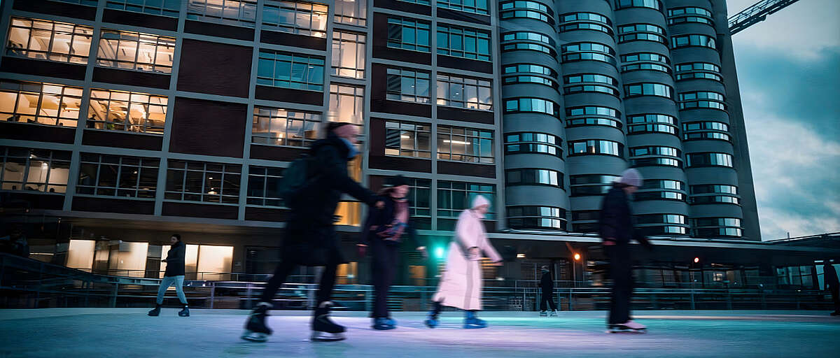 Menschen laufen Schlittschuh auf der Eisfläche vor den Gebäuden der Bremer Überseeinsel am Abend